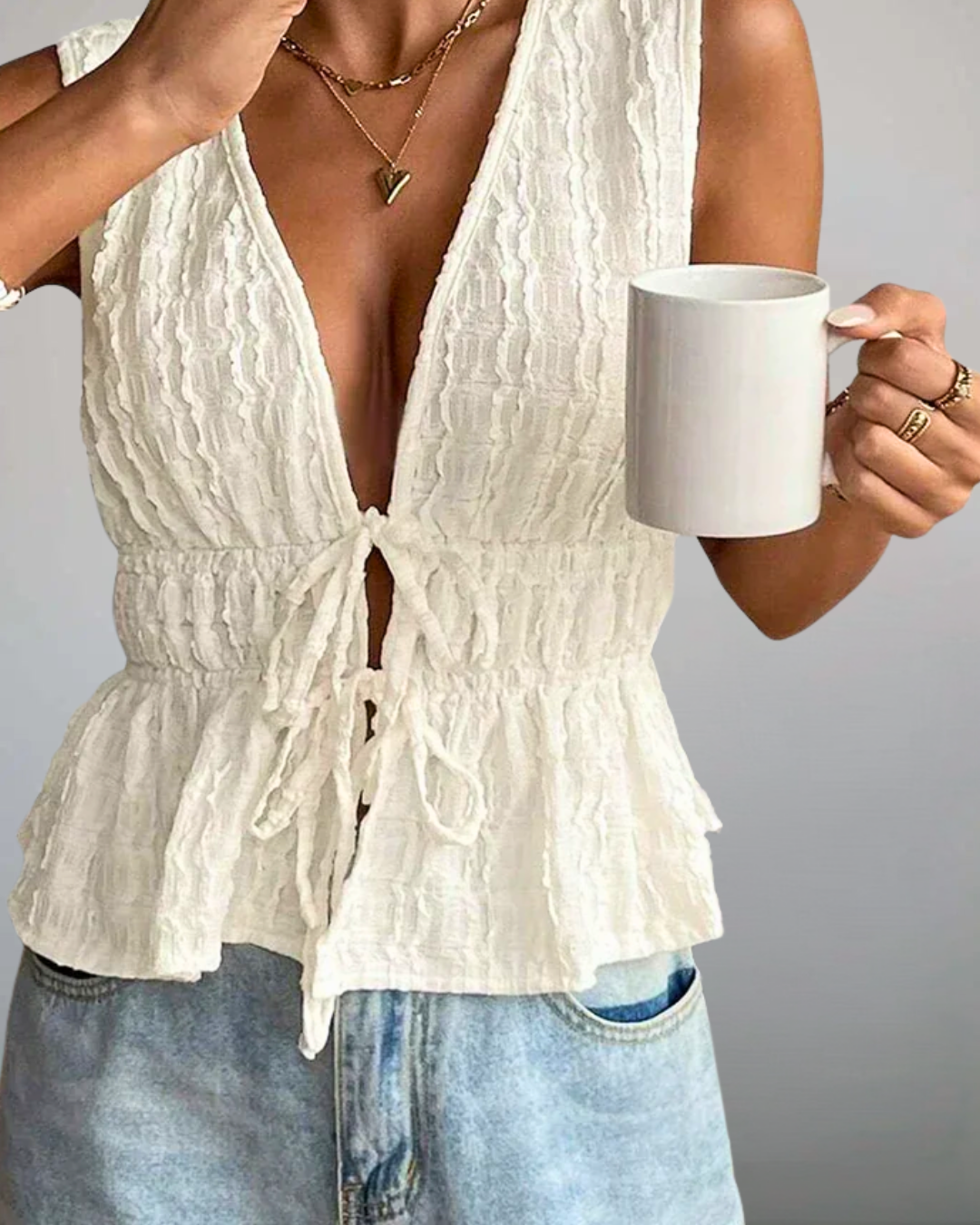 Person wearing a white textured top and blue jeans, holding a white mug.